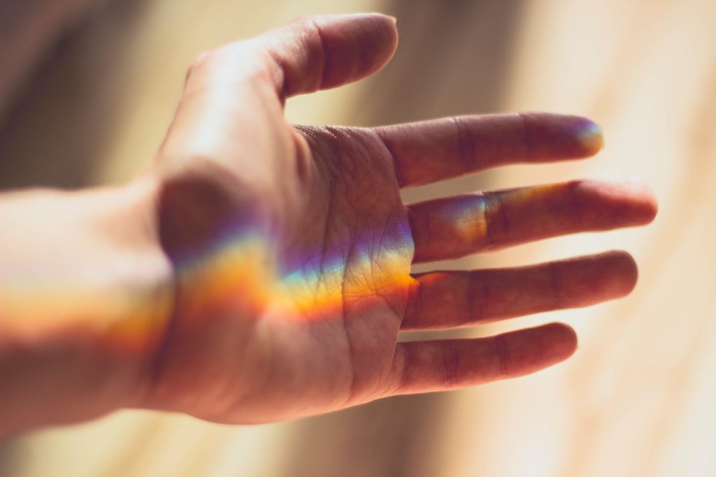 Outreached hand with a rainbow reflection on the palm of it. 